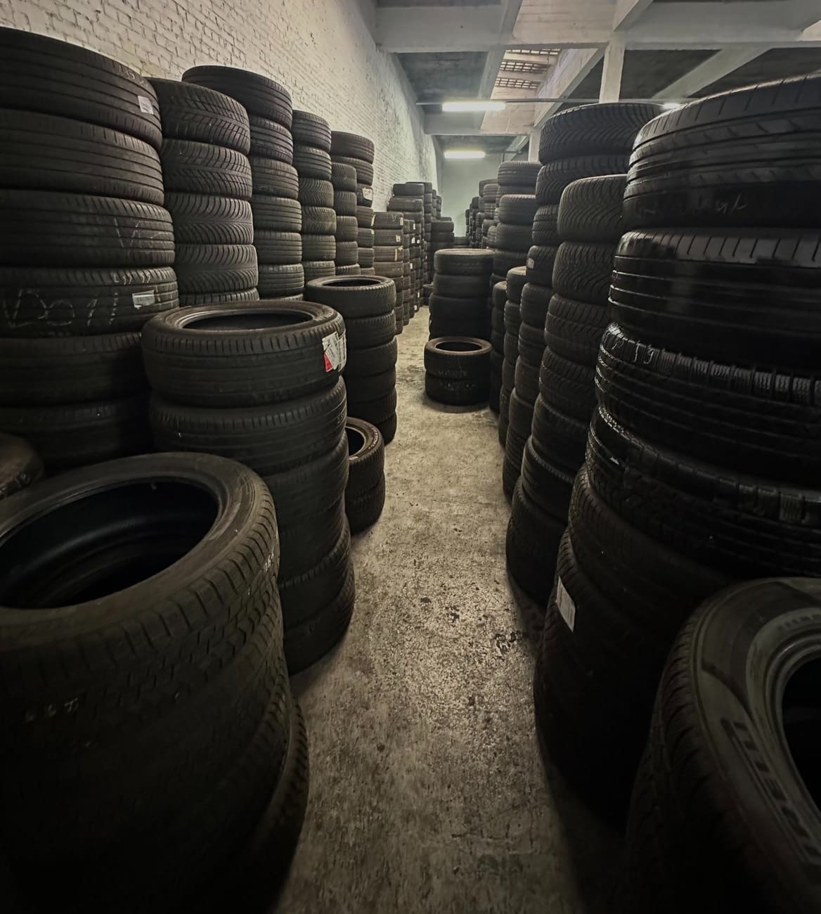 Allée entre de hautes piles de pneus dans l'entrepôt de pneus de WeFix Auto's.