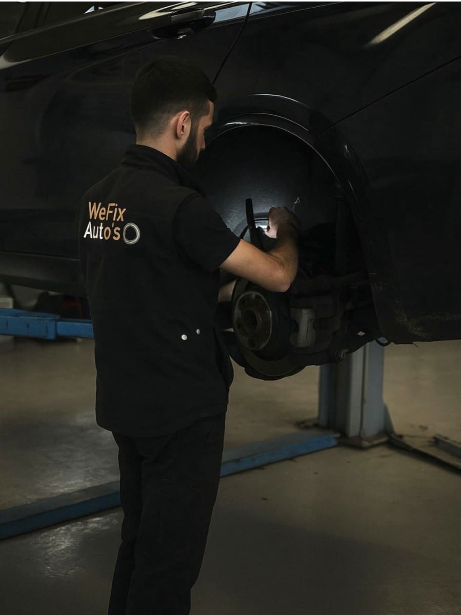 Technicien en tenue de travail WeFix Auto's travaillant sur le frein d'une voiture sur le pont élévateur.